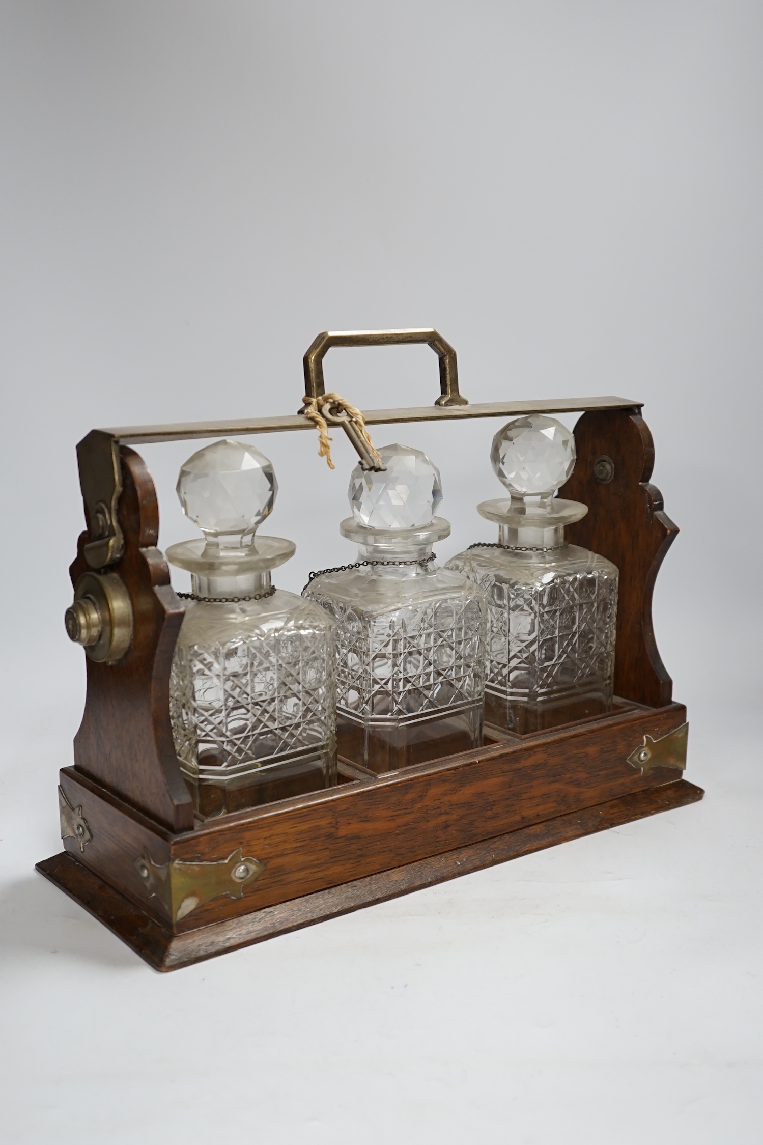 An oak three bottle electroplate tantalus, 29.5cm high